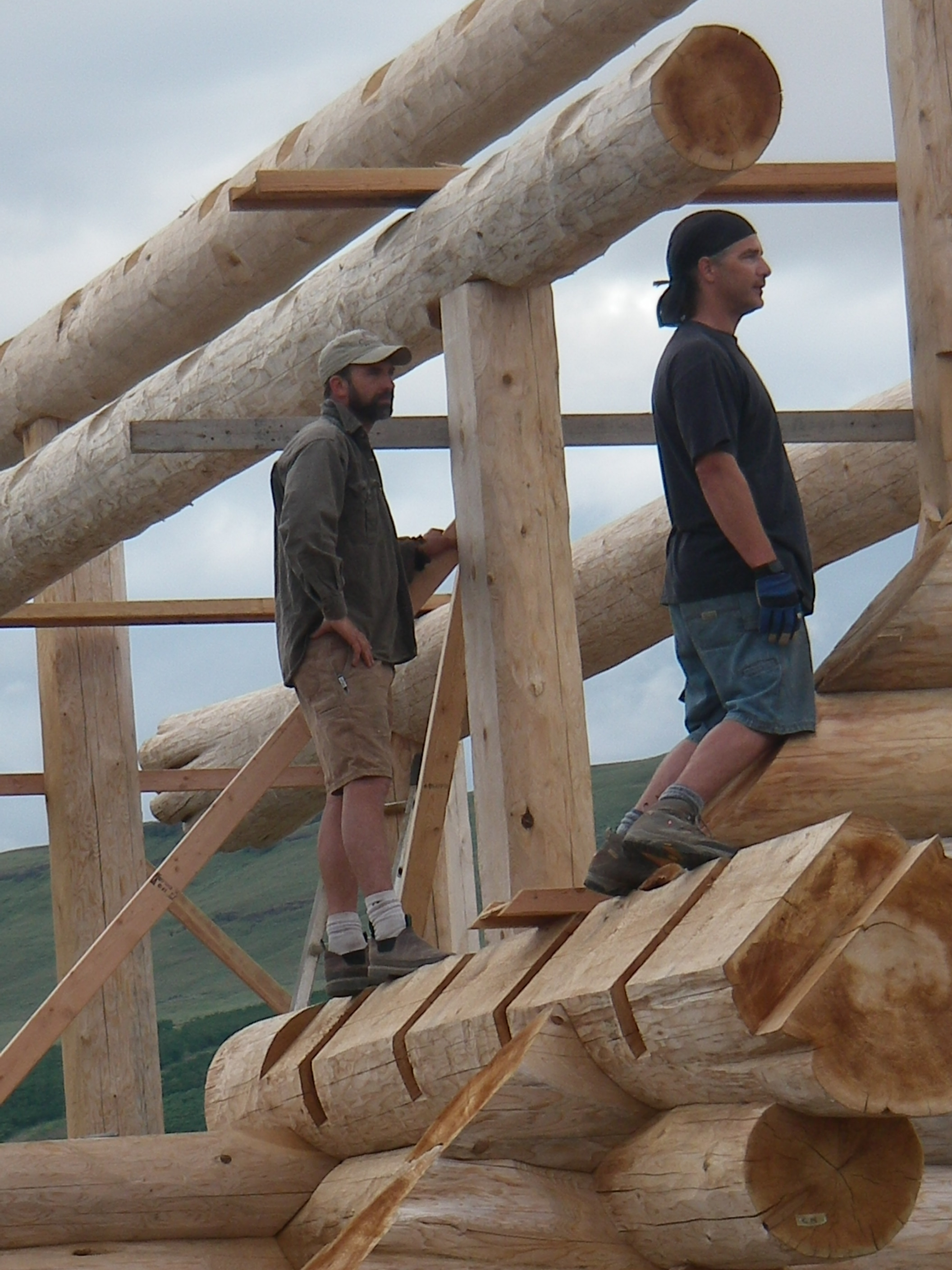 two men on top of logs in new construction of a log home